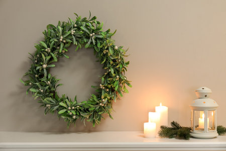 Lantern, fir branches with candles on mantelpiece and hanging Christmas wreath in roomの写真素材