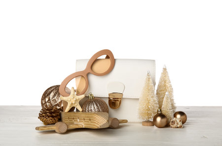 Bag with sunglasses, wooden airplane and Christmas decor on table against white background