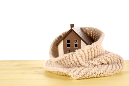 House model with scarf on yellow wooden table against white background. heating conceptの写真素材