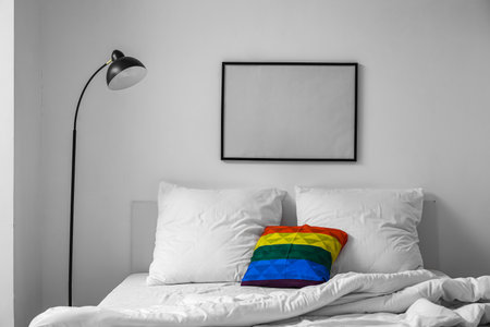 Comfortable bed with rainbow pillow in light roomの写真素材