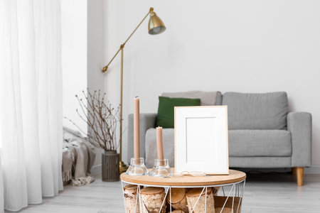 Blank frame with candles and eyeglasses on table in living room