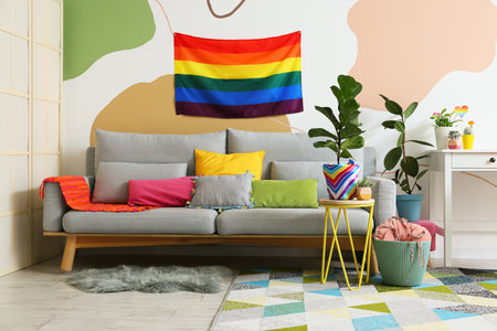 Comfortable sofa, houseplants and rainbow flag hanging on color wallの写真素材