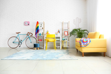 Comfortable sofa and workplace with bicycle and rainbow flags near white brick wallの写真素材