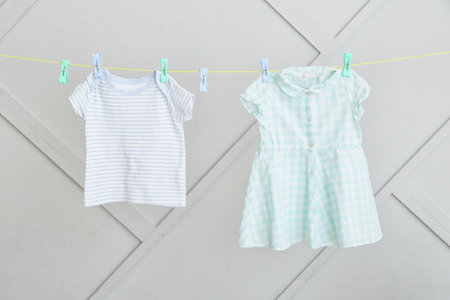 Baby clothes hanging on rope against gray wall