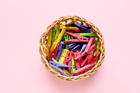 Basket with plastic clothes pins on pink background