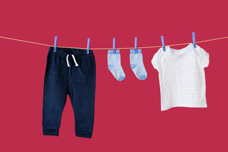 Baby clothes hanging on laundry line on color backgroundの写真素材