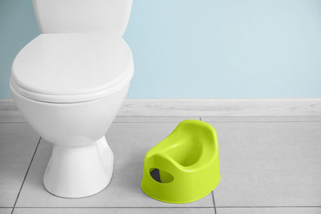 Potty and toilet bowl on gray tile floor near color wall