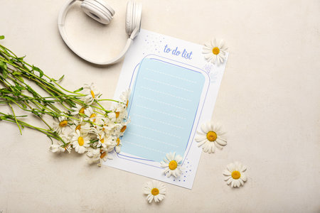 Blank to do list, headphones and chamomile flowers on light background