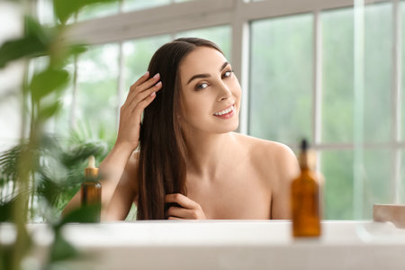 Smiling woman applying essential oil on hair in bathroomの写真素材