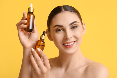 Beautiful woman with healthy skin holding bottles with essential oil on color backgroundの写真素材