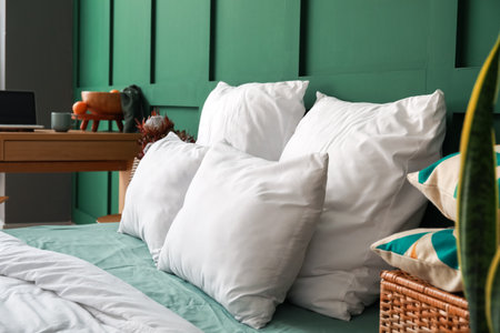Comfortable bed with soft pillows near green wall, closeupの写真素材
