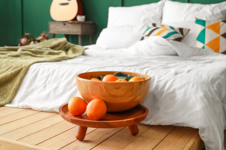 Wooden bowl with oranges near comfortable bed with soft linesの写真素材