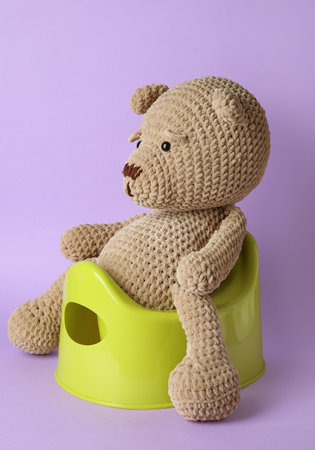Cute toy bear sitting on potty on color backgroundの写真素材