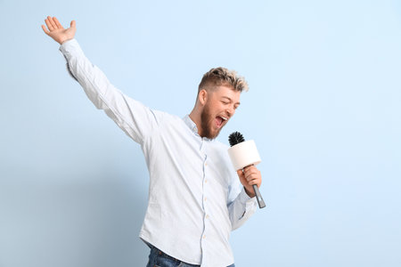 Funny young man with toilet brush and paper singing on color backgroundの写真素材
