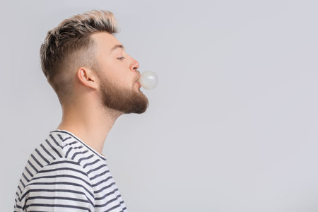 Young man chewing gum on light backgroundの写真素材