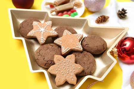 Plate in shape of Christmas tree with treats and decor on yellow background, closeup