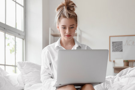 Morning of beautiful young woman using laptop on bedの写真素材