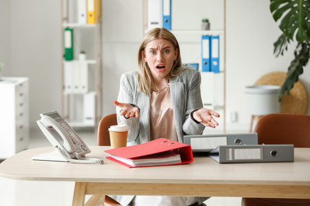Angry young woman with folders at table in officeの写真素材