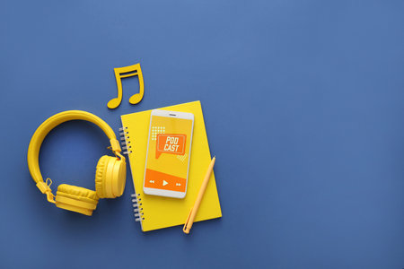 Mobile phone with word PODCAST on screen, notebook and headphones on blue backgroundの写真素材