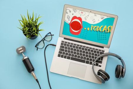 Modern laptop with word PODCAST on screen, microphone, eyeglasses and headphones on color backgroundの写真素材