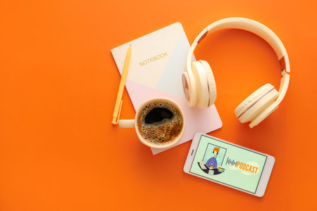 Headphones, mobile phone with word PODCAST on screen, notebook and cup of coffee on color backgroundの写真素材