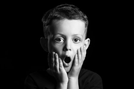 Black and white portrait of surprised little boy on dark backgroundの写真素材