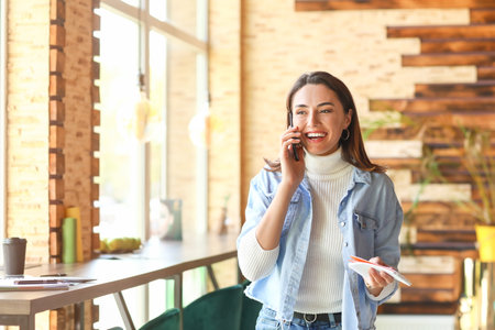 Beautiful business owner talking by mobile phone in her cafeの写真素材