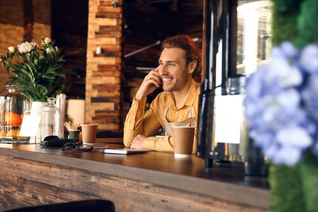 Young business owner talking by mobile phone at table in his cafeの写真素材