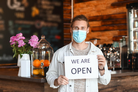 Male business owner with medical mask and opening sign in his cafeの写真素材