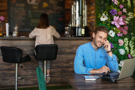 Handsome business owner talking by mobile phone at table in his cafeの写真素材