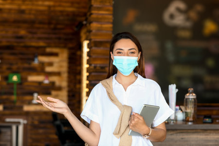 Female business owner with medical mask and tablet computer in her cafeの写真素材