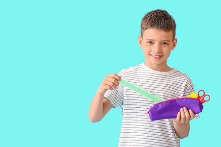 Little boy holding pencil case with stationery on color background
