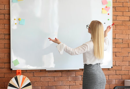 Young female teacher conducting lesson near whiteboard in classroomの写真素材