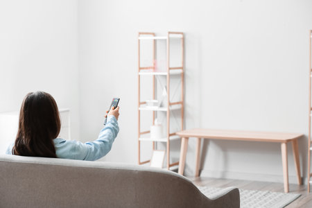 Woman with TV remote control sitting on sofa at homeの写真素材