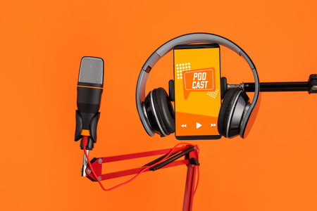 Modern microphone with headphones and mobile phone with with podcast playlist on screen against color backgroundの写真素材