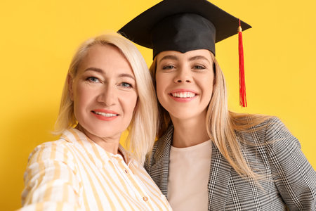 Happy female graduation student with her mother on color backgroundの写真素材