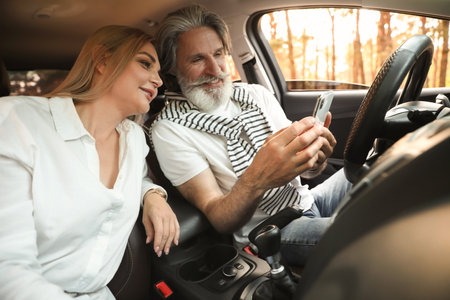 Happy mature couple using mobile phone in carの写真素材