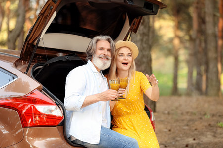 Happy mature couple drinking juice near car in forestの写真素材