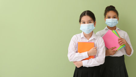 Cute little schoolgirls wearing medical masks on color backgroundの写真素材