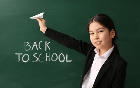 Cute Asian schoolgirl with paper airplane near blackboard in classroomの写真素材