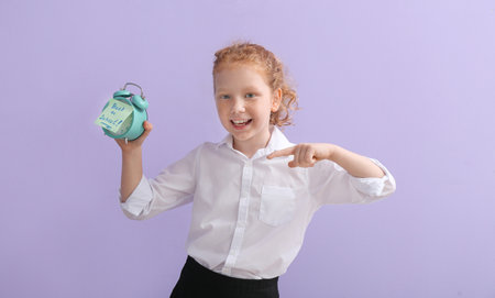 Cute little schoolgirl with alarm clock on color background