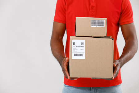 African-American delivery man with parcels on gray background
