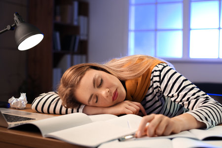Tired female student sleeping at table late in the eveningの写真素材