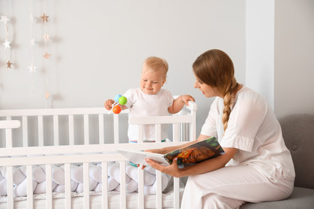 Mother reading book to her cute little baby in cribの写真素材