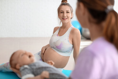 Young pregnant woman with trainer and little baby at gymの写真素材