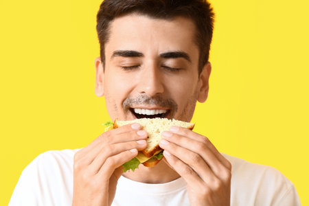 Young man eating tasty sandwich on color backgroundの写真素材
