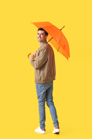 Handsome young man with umbrella on color backgroundの写真素材