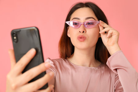 Stylish young Asian woman taking selfie on color backgroundの写真素材