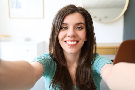 Beautiful young woman taking selfie at homeの写真素材
