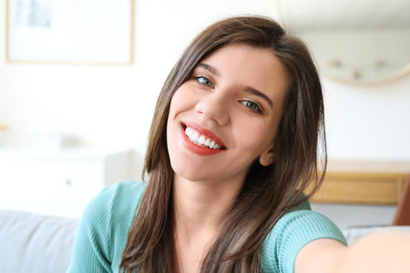 Beautiful young woman taking selfie at homeの写真素材